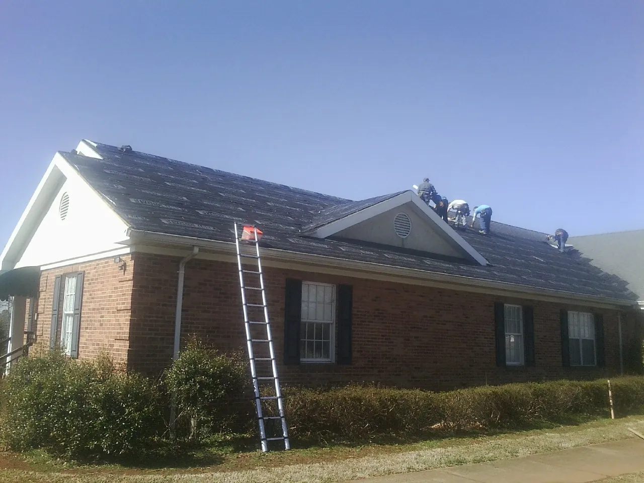 Crew tearing shingles off a brick ranch roof with a ladder set — Metal Roof Repair work by our crew in Peoria
