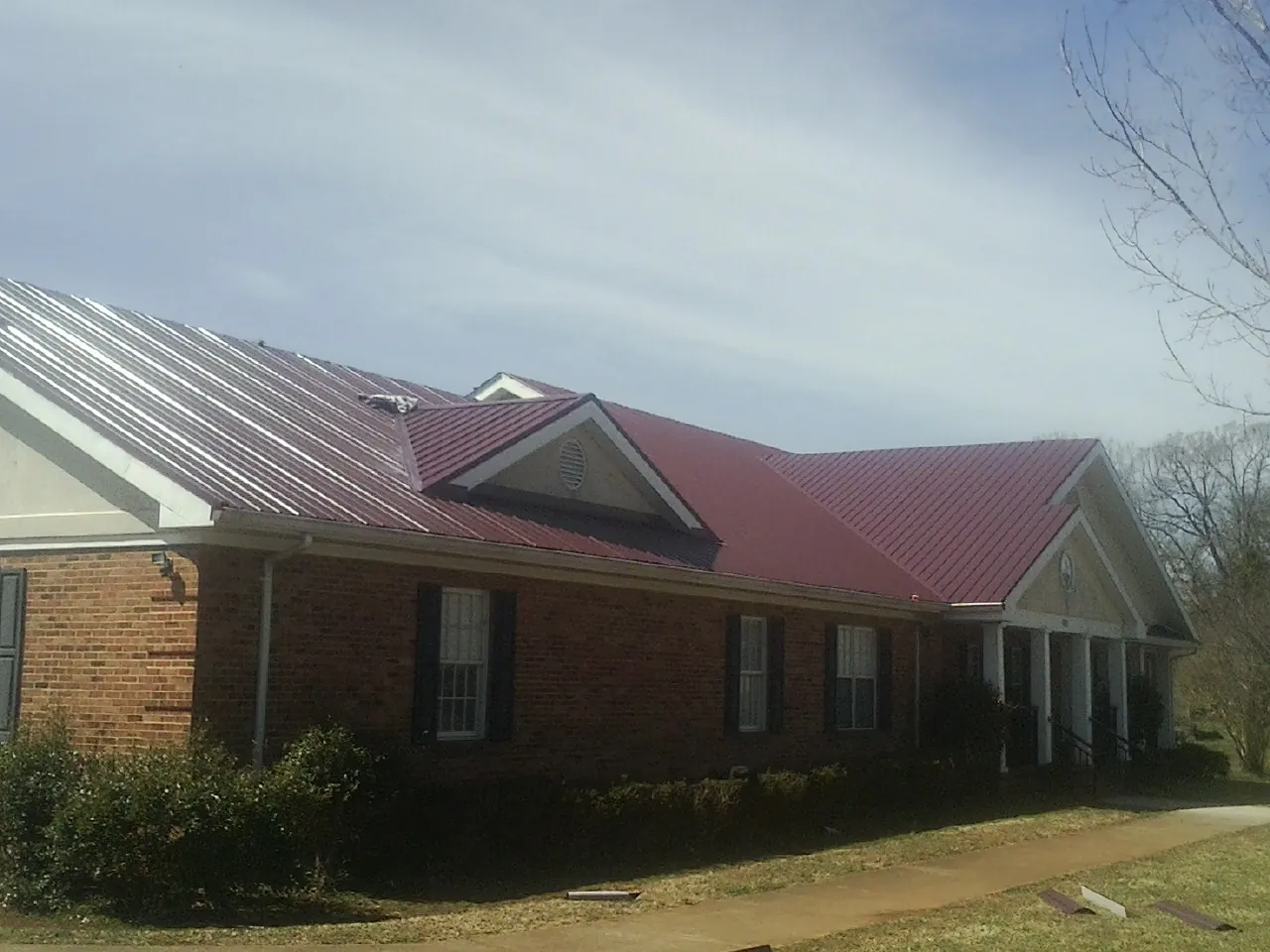Red metal roof with gabled entries on a long brick building, from a Hail Damage Roof Repair job in Peoria