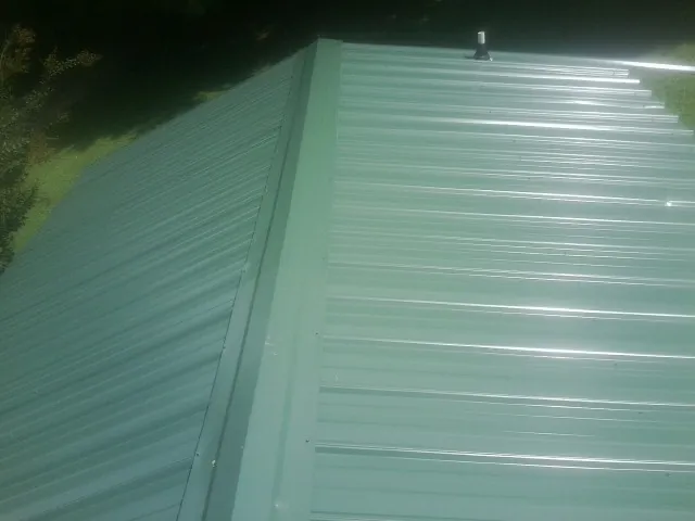 New green metal panels meeting at the ridge of a roof — Flat Roof Repair work by our crew in Peoria