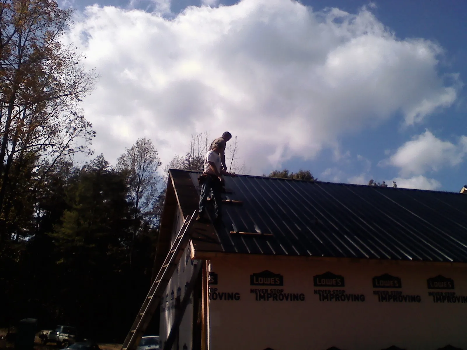 Roofer fastening dark metal panels high against a cloudy sky, from a Roof Inspection job in Peoria